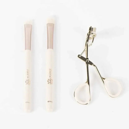 Due pennelli make-up Marie Disney e un piegaciglia su sfondo bianco, accessori trucco Nerdscape.
